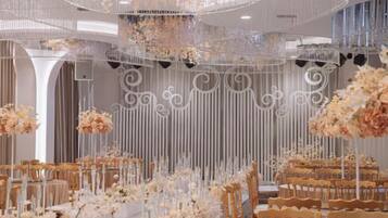 A banquet hall with tiered seating, floral arrangements, and decorative lighting fixtures.
