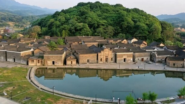 Ein traditionelles Dorf mit einem zentralen Teich, umgeben von gleichförmigen Gebäuden mit geneigten Dächern.