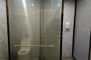A glass-enclosed shower stall with a towel rack and a power outlet on the wall.
