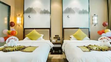 Quarto de hotel com duas camas, cada uma com roupa de cama branca e almofadas amarelas. Há luminárias na parede e um quadro com montanhas.