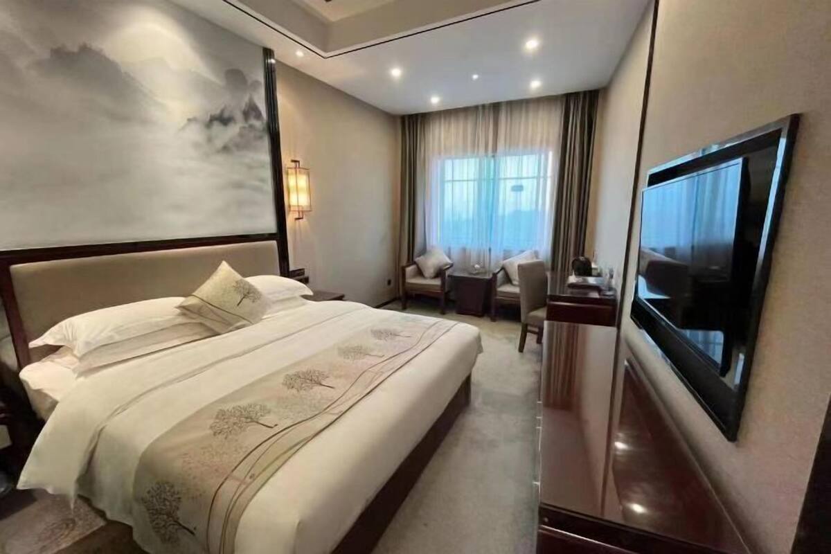 Une chambre d’hôtel avec un grand lit, un bureau avec une chaise, une télévision et une fenêtre avec des rideaux.