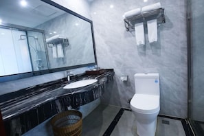 A modern bathroom with a marble countertop, a white toilet, a glass shower enclosure, and a large mirror.