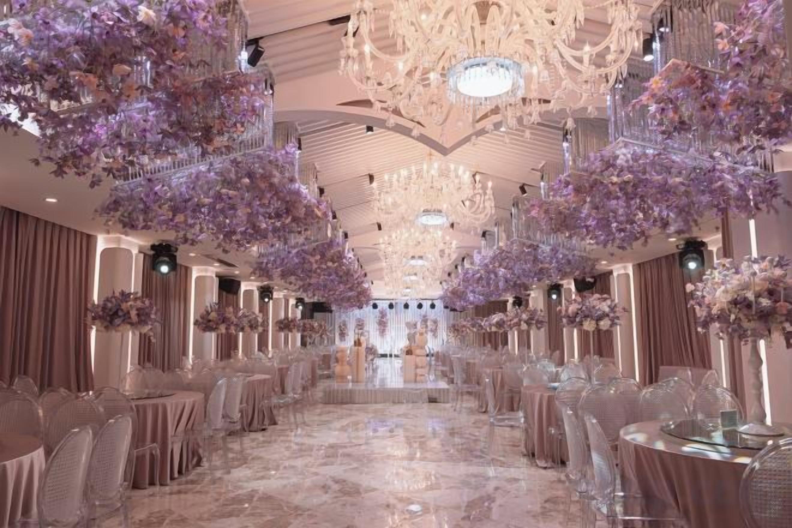 A banquet hall with round tables, chairs, and hanging floral arrangements.