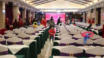 A banquet hall with rows of tables and chairs, a stage with a pink backdrop, and people in red attire.