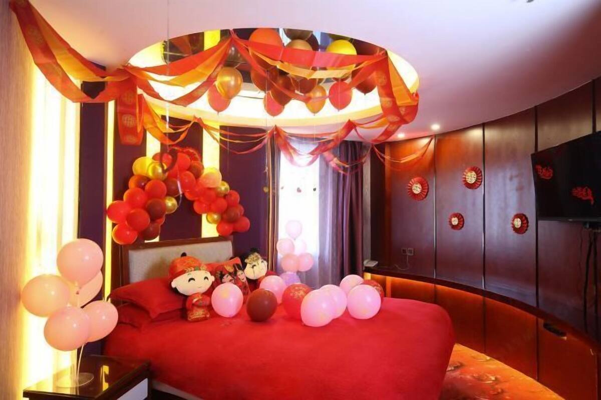 Une chambre d’hôtel avec un lit rouge, des ballons décoratifs et une horloge murale.