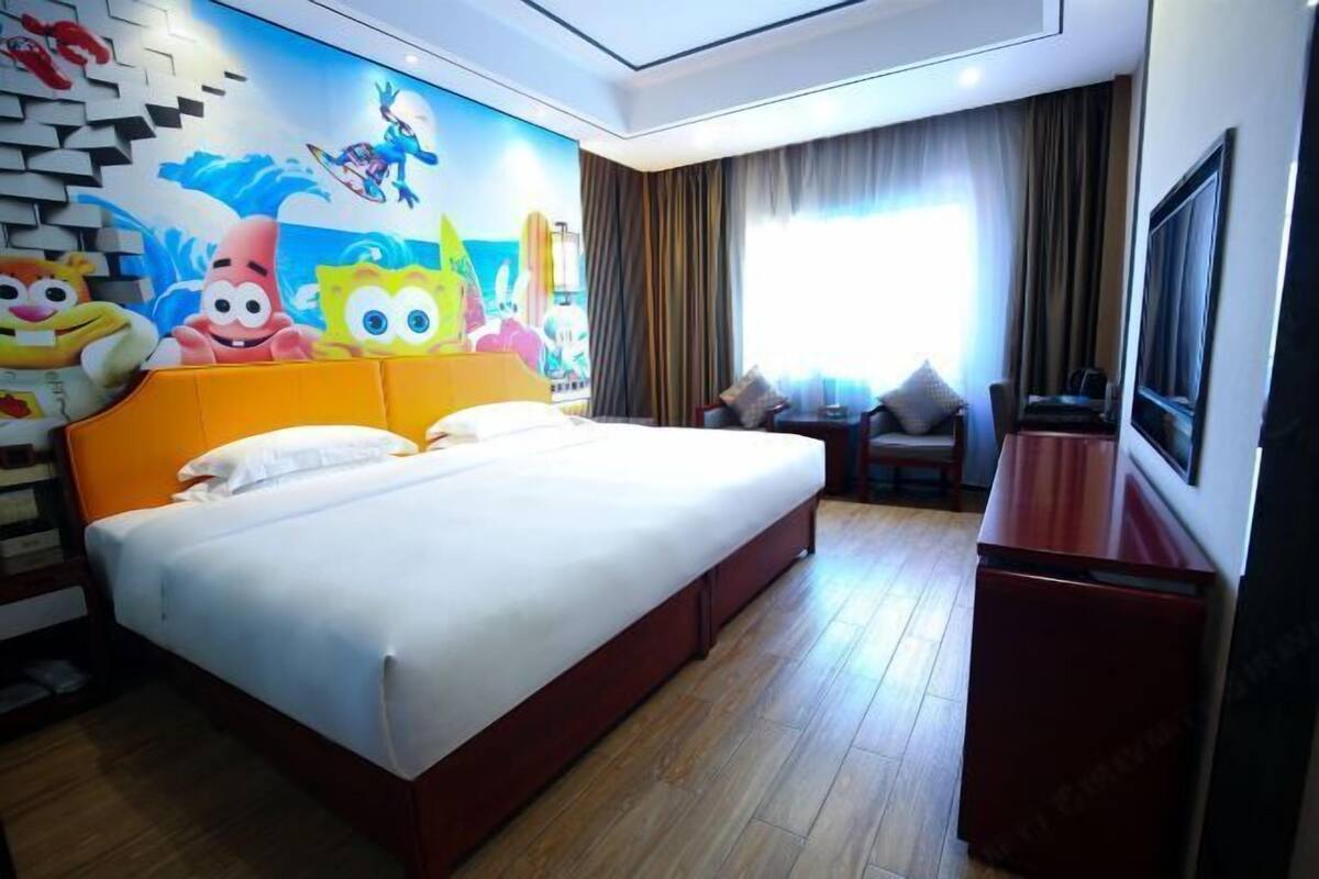 Une chambre d’hôtel avec un grand lit, une télévision, un bureau et une fresque murale représentant des personnages de dessins animés.