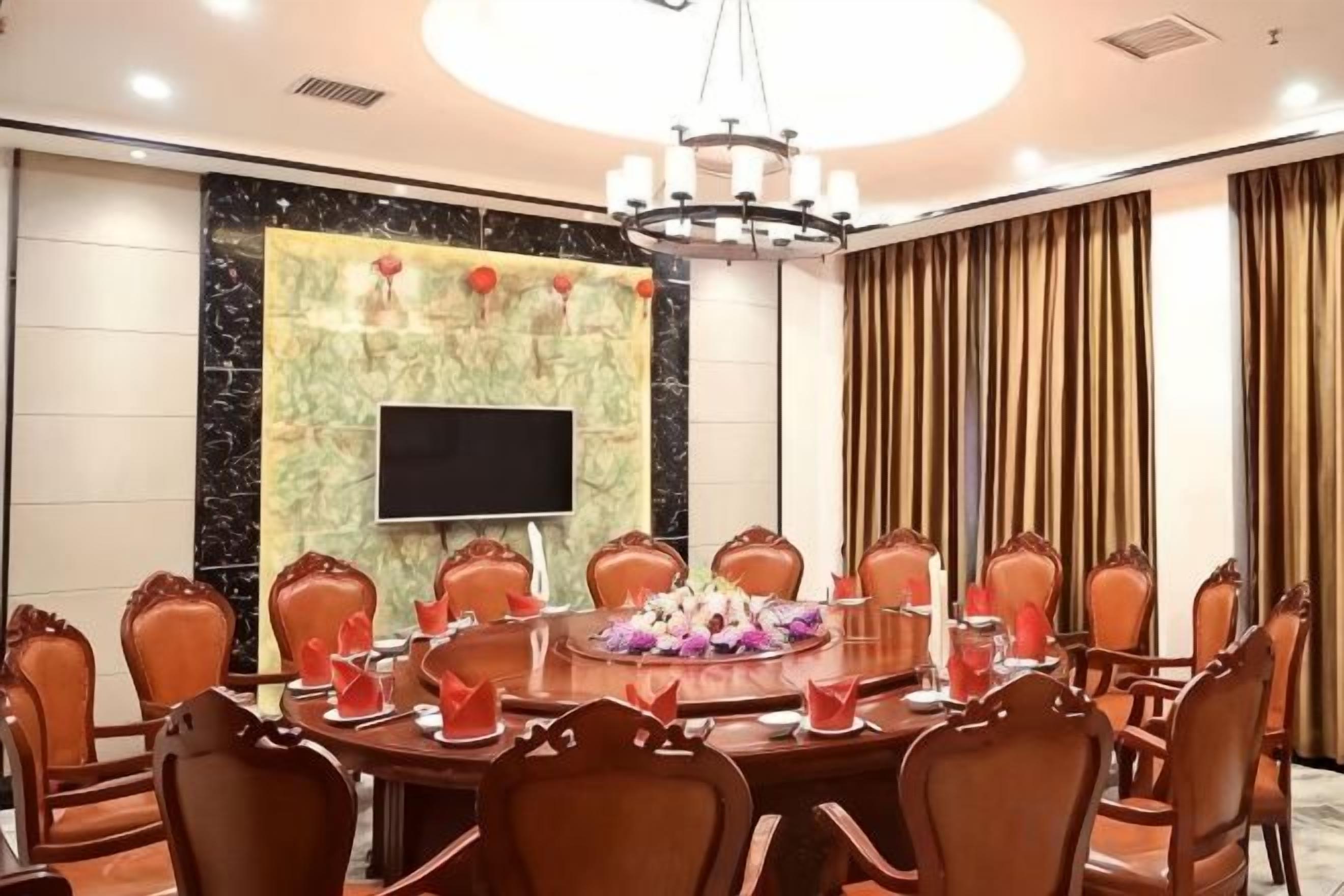 Une salle de conférence équipée d’une table ronde, de chaises, d’un écran de télévision et d’un lustre.