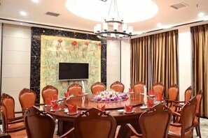 A conference room with a round table, chairs, a TV screen, and a chandelier.