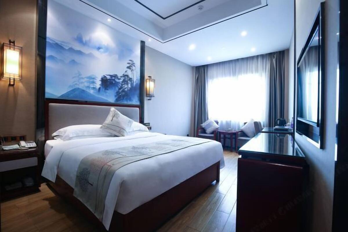 Une chambre d’hôtel avec un grand lit, un bureau, une chaise, une télévision et un tableau au mur.