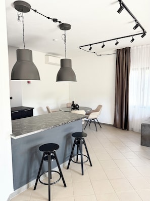 Une cuisine moderne dotĂ©e dâun Ăźlot central, de tabourets de bar, de luminaires suspendus et dâun coin repas avec des chaises.
