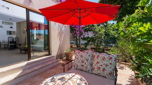 Un patio con un paraguas rojo, una mesa redonda con diseño de mosaico y un sofá con cojines estampados.