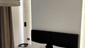 Una habitación de hotel moderna con una cama grande, un cabecero negro y una mesita de noche pequeña.