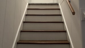 Eine Treppe mit Holzstufen und einer Handläufe, die zu einer Tür führt, an deren Wand eine gerahmte amerikanische Flagge hängt.