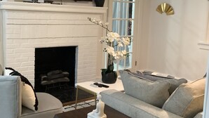 Ein Wohnzimmer mit einem weißen Kamin, einem darüber montierten Flachbildfernseher, einer Couch, einem Couchtisch und Wanddekoration.