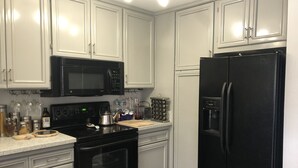 Una cocina con armarios blancos, una estufa negra, un microondas negro y un refrigerador negro.