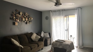 Una sala de estar con un sofá de color oscuro, una alfombra estampada, un ventilador de techo y un adorno de pared.
