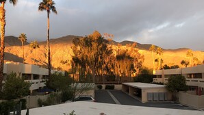 Un hotel con estacionamiento, palmeras y montañas al fondo.