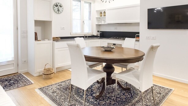 Une cuisine moderne avec des meubles blancs, une table à manger avec des chaises, un lustre et un téléviseur à écran plat.