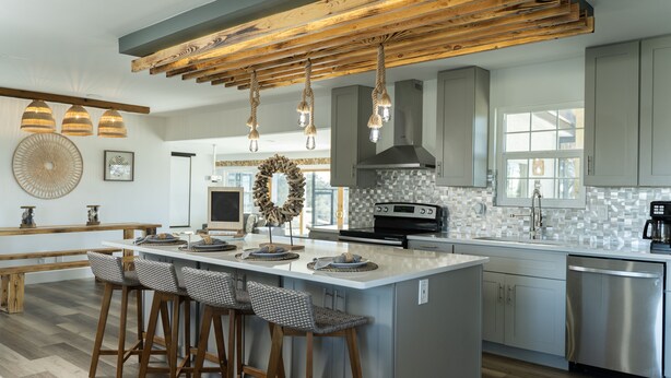 A modern kitchen with a large island, bar stools, hanging pendant lights, and a rustic wooden ceiling. - beautiful country house (Clermont)