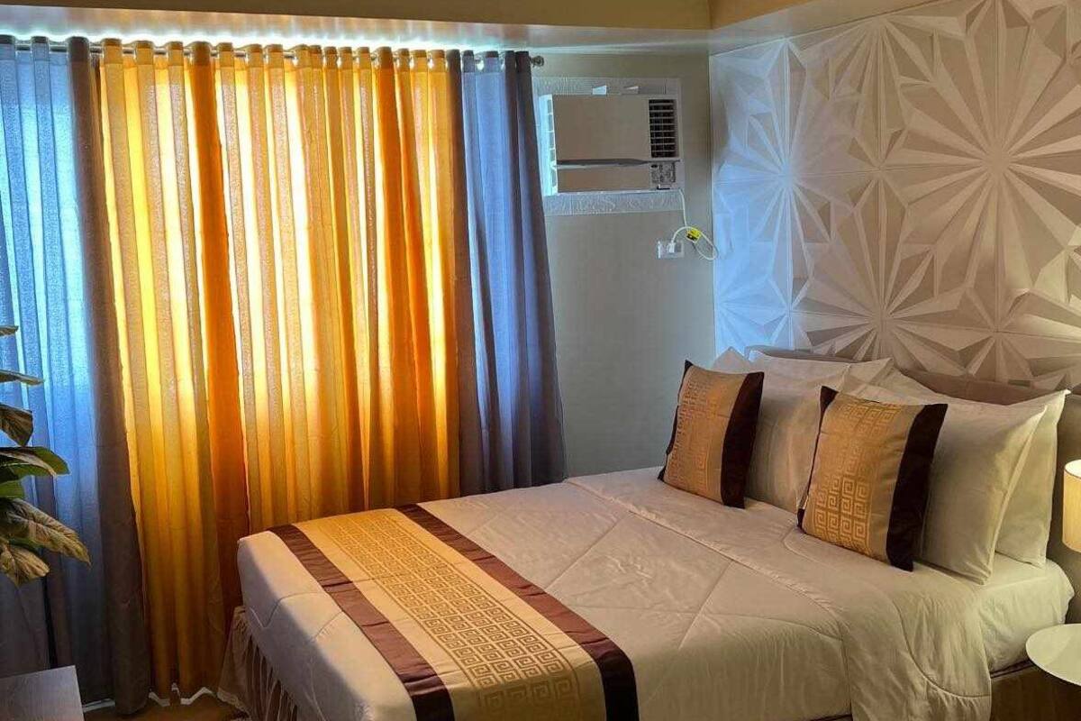A hotel room with a large bed, a bedside table, a lamp, and a decorative wall panel.