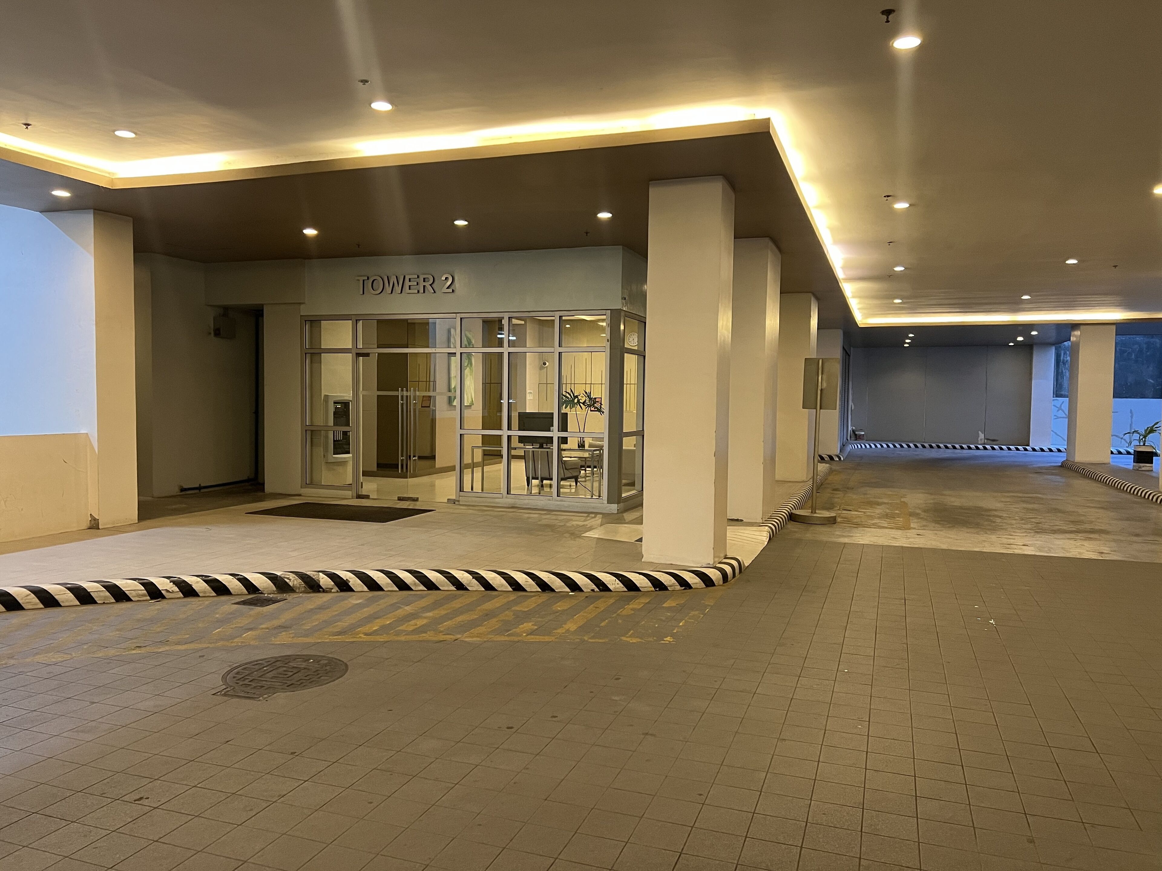 Entrada de hotel con un letrero que dice "TOWER 2", puerta de cristal y suelo de baldosas con un borde a rayas.