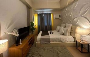 A hotel room with a bed, a TV on a wooden stand, a bedside table with a lamp, and a decorative plant. - Avida Tower Davao  (Davao)