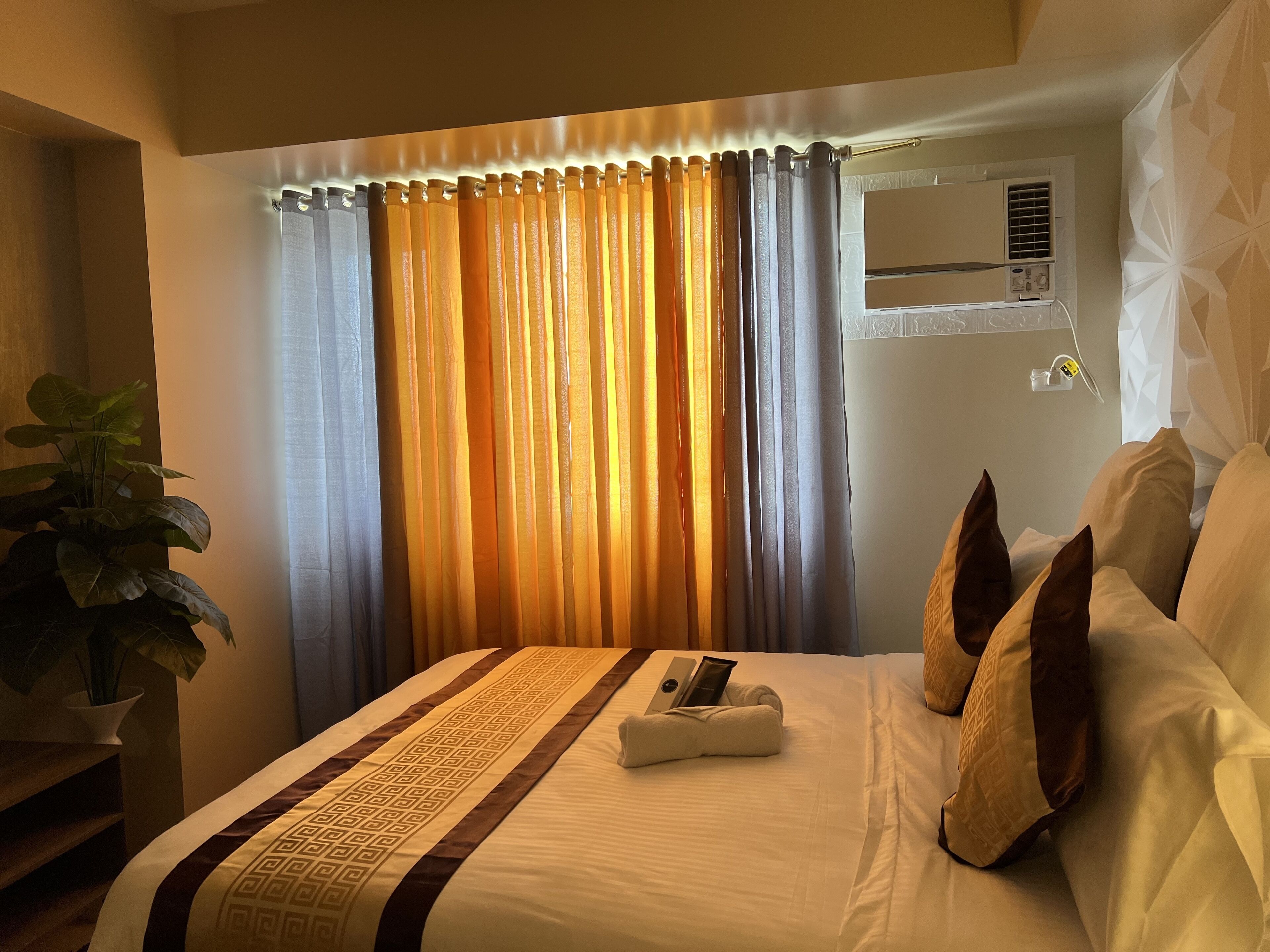 Ein Hotelzimmer mit einem Bett, einer Zimmerpflanze und einem Fenster mit Vorhängen.