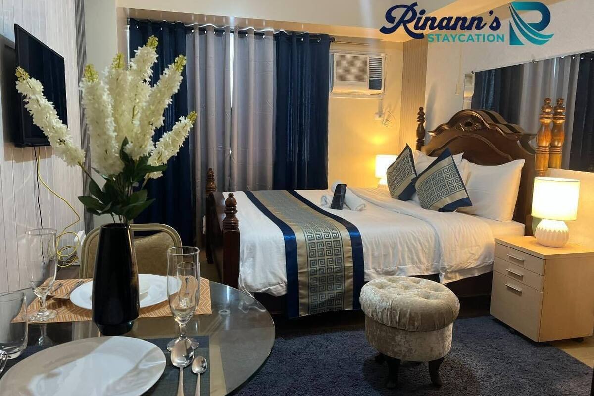 A hotel room with a bed, bedside table, lamp, and a dining area with a table set for two.
