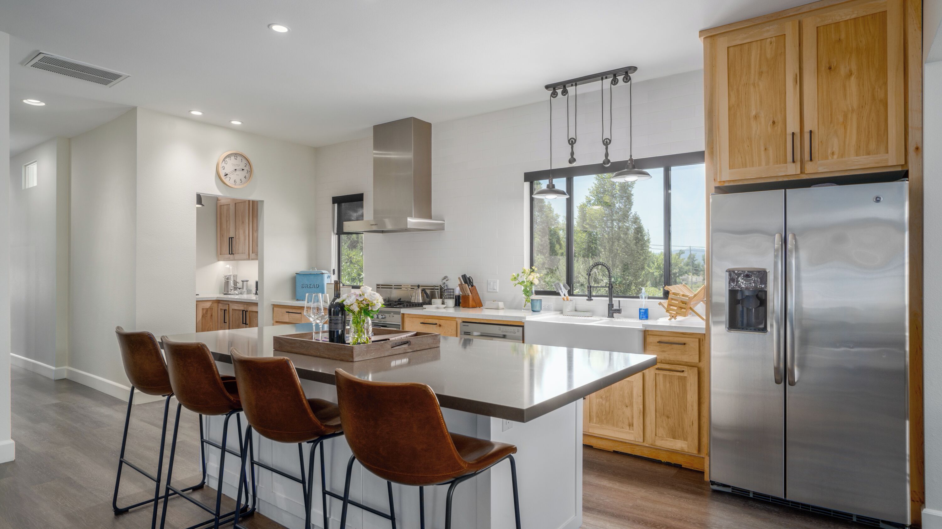 A modern kitchen with a central island, wooden cabinets, stainless steel appliances, and a large window providing natural light.