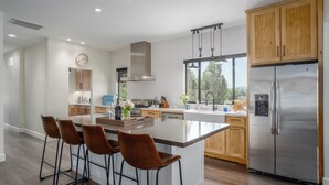 Une cuisine moderne dotée d’un îlot central, de meubles en bois, d’appareils électroménagers en acier inoxydable et d’une grande fenêtre qui laisse entrer la lumière naturelle.