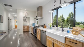 Une cuisine moderne avec des meubles en bois, des appareils électroménagers en acier inoxydable et une grande fenêtre donnant sur un paysage verdoyant.