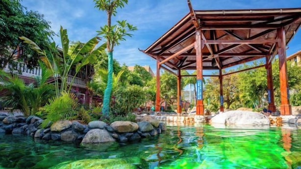 Un pabellón de madera sobre una piscina cristalina, con rocas y plantas tropicales a su alrededor.
