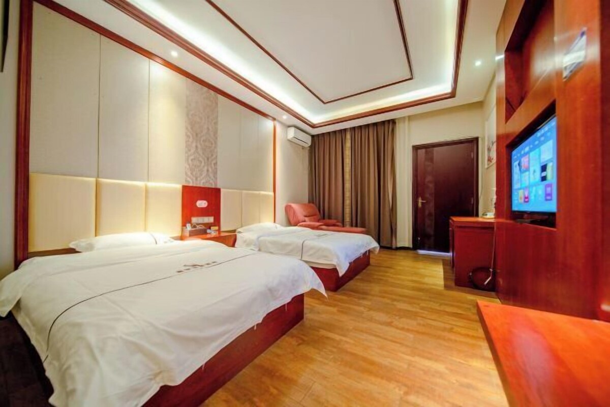 A hotel room with two beds, a TV, a desk, and a red chair.
