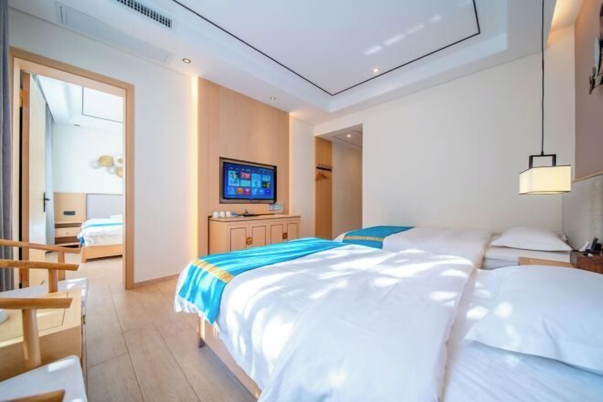A modern hotel room with a large bed, a desk, a television, and a view of the hallway.