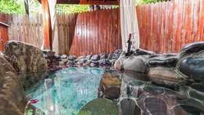 Una piscina cristalina con rocas y una botella, rodeada por una valla de madera y una pérgola.