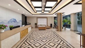 Un vestíbulo de hotel con una recepción, una alfombra estampada, una cama grande y un diseño moderno de techo.