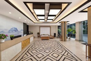A hotel lobby with a reception desk, a patterned carpet, a large bed, and a modern ceiling design. - Xinjia Yuquan Hot Spring Hotel (Mile)