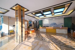 A hotel lobby with a reception desk, seating area, and a patterned floor. - Xinjia Yuquan Hot Spring Hotel (Mile)