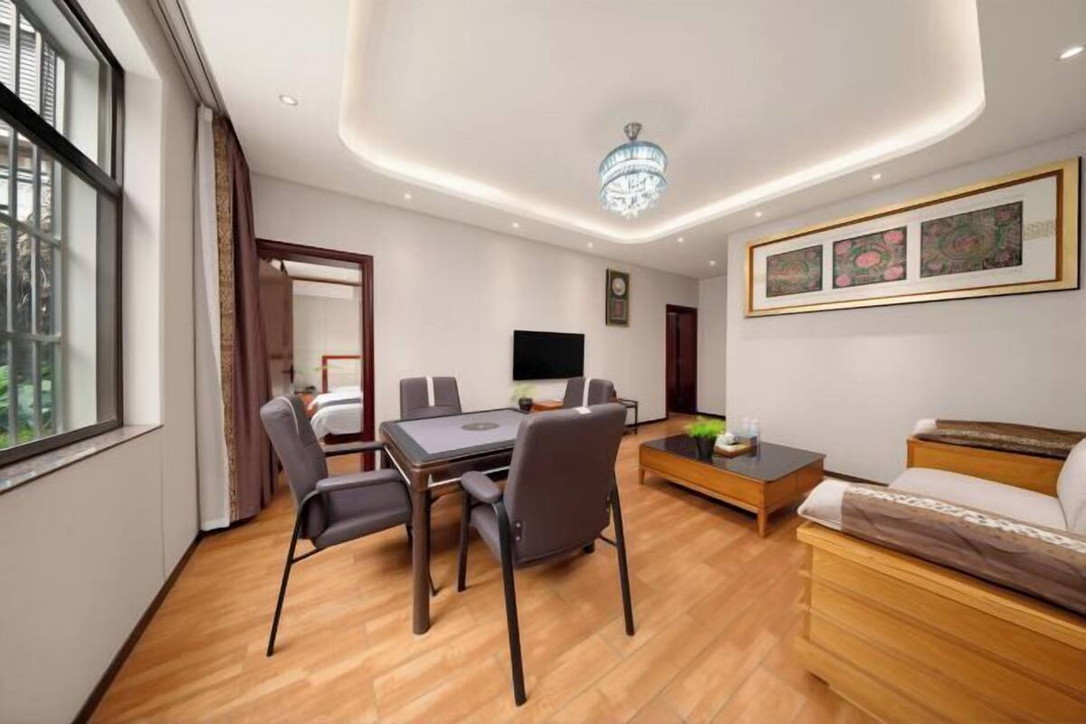 Moderni hotellihuone, jossa on ruokapöytä, tuoleja, sohva, televisio ja taideteoksia seinällä.