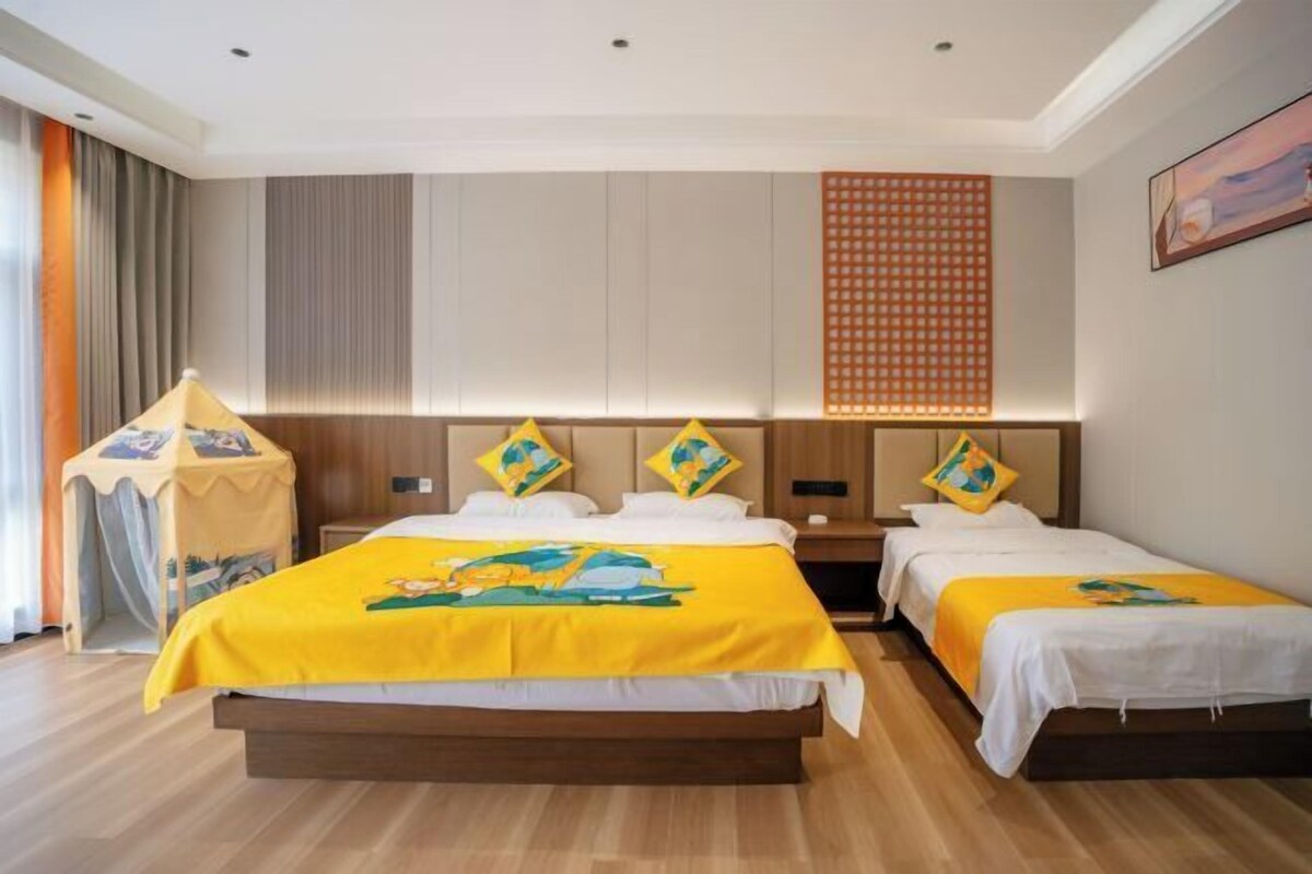 A hotel room with a large bed, two smaller beds, a wooden floor, a wall-mounted TV, and a curtain on the left.