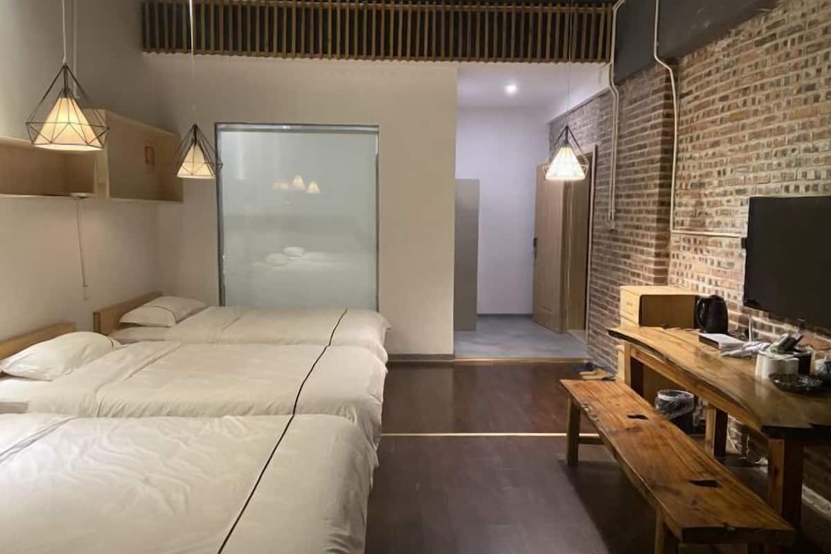 Una habitación de hotel moderna con dos camas, un banco de madera, un televisor y una pared de ladrillo.