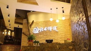 Zona de recepción con pared de piedra, mostrador de madera y un cartel con caracteres chinos.
