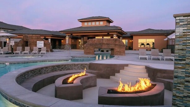 A resort with a swimming pool, fire pits, lounge chairs, and a building with a unique rock arch entrance.