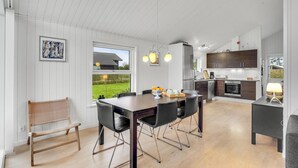 A modern kitchen with dark wooden cabinets, a stainless steel refrigerator, and a built-in oven. There is a dining area with a wooden table and black chairs.
