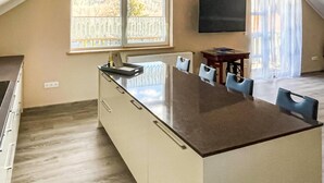 A modern kitchen with a central island, a dining area with chairs, a TV mounted on the wall, and a window with a view of trees. - Cozy apartment in Jelesnia with WiFi (Jelesnia)