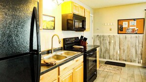 Una cocina con armarios de madera, un refrigerador negro, un microondas y una estufa.
