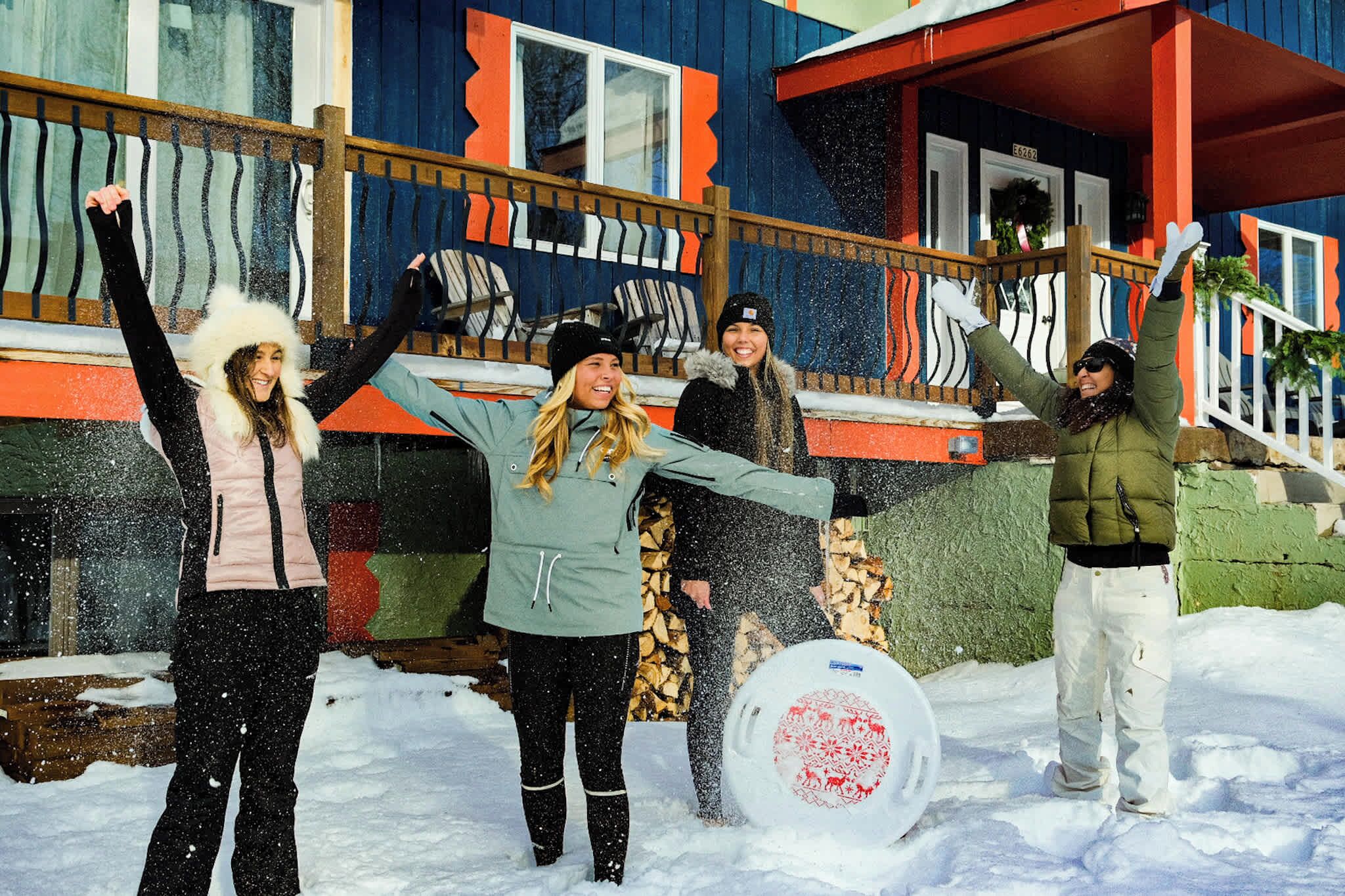 A group of people standing in the snow in front of a building with a colorful exterior and a wooden deck.