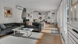 En moderne stue med sofa, sofabord og kunst. Der er et køkkenområde med et spisebord og stole i baggrunden.