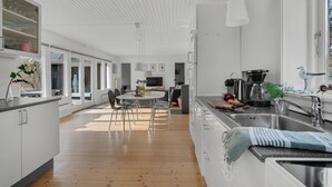Et moderne køkken med en central ø, et spiseområde med et rundt bord og en opholdsstue med sofa og fjernsyn.