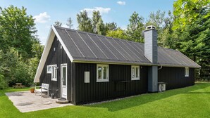 En sort metalbygning med skråt tag, skorsten og en lille veranda med et bord og stole.